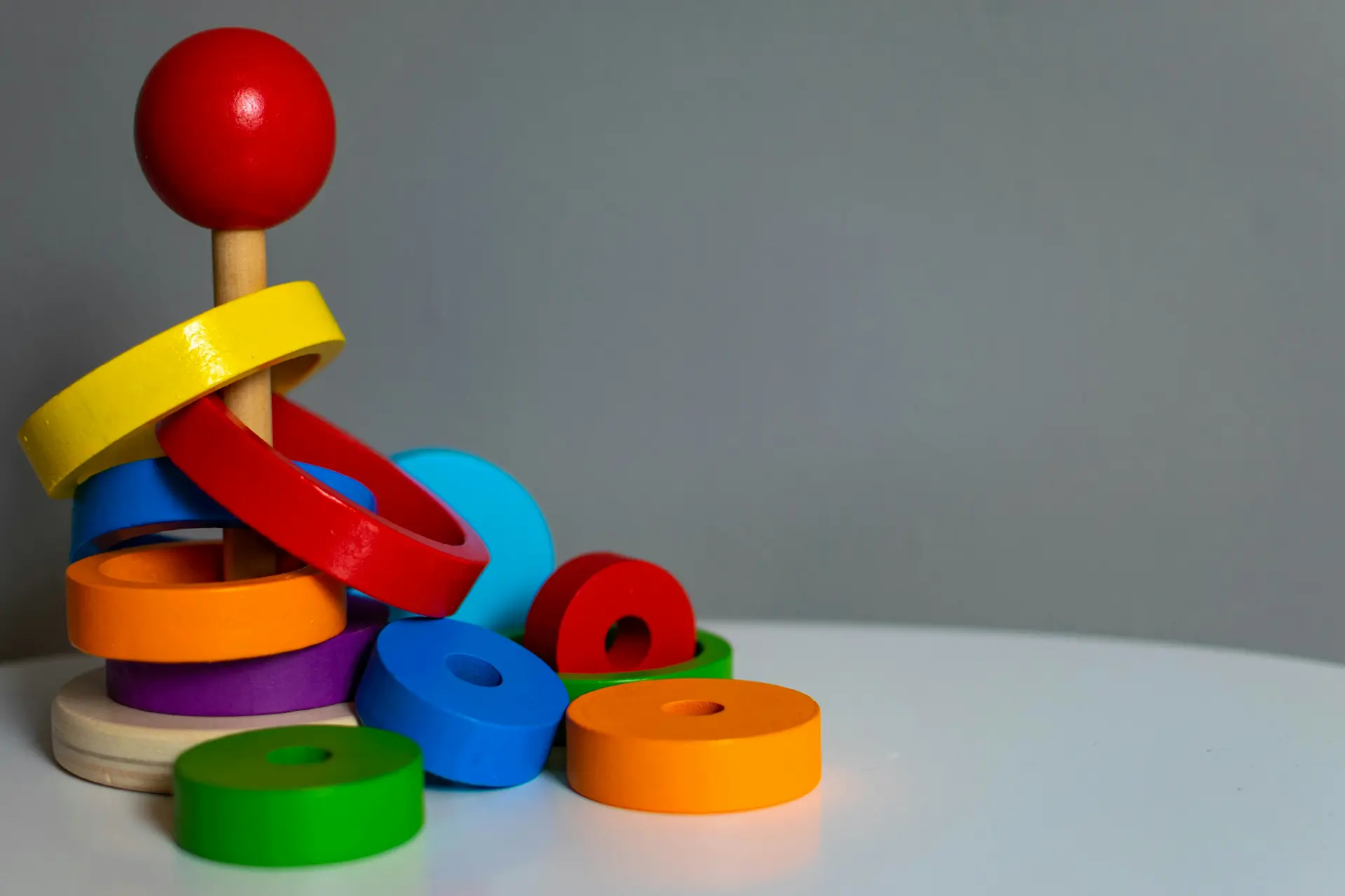 Wooden ring stacking toy with colourful discs loosely stacked and scattered - Photo by Tomas Petz on Unsplash
